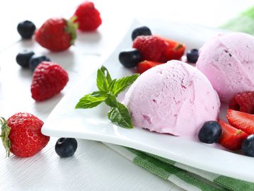 Two scoops of pink ice cream with fresh strawberries and blueberries.