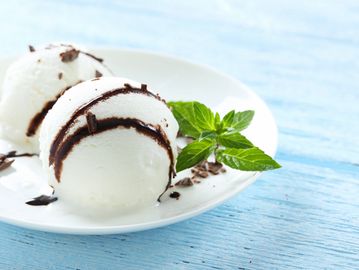 Two scoops of vanilla ice cream with chocolate syrup and a mint garnish on a white plate.