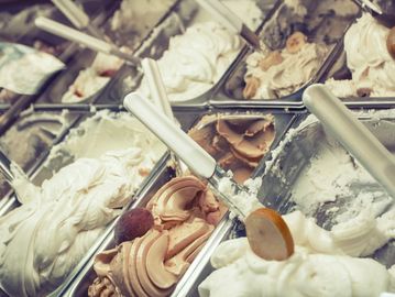 Various flavors of gelato displayed in metal trays with scoops.