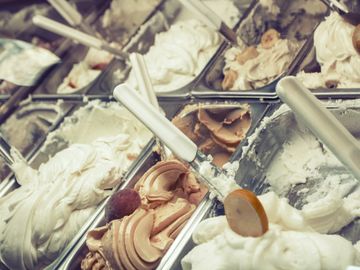 Various flavors of gelato displayed in metal trays with scoops.