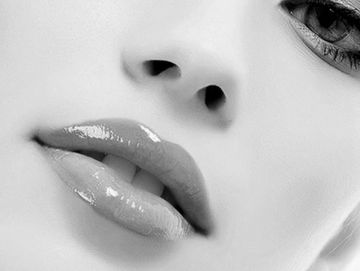 Close-up of glossy lips and part of the nose in black and white.