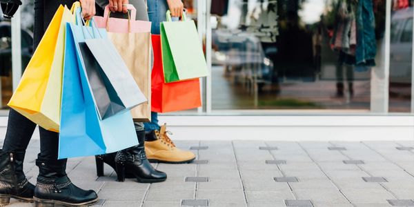 People walking along the street of shops holding onto colourful shopping bags. the image only shows 