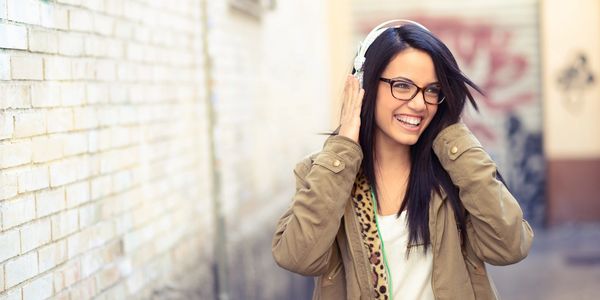 A young woman enjoys music with headphones, smiling joyfully outdoors.