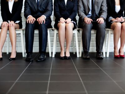 Five professionals seated in a row, dressed formally, waiting.