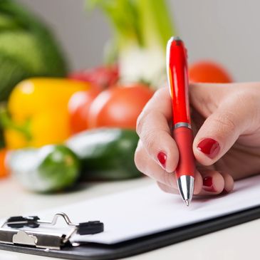 Woman with red nails recording nutrition information with vegetables in the background