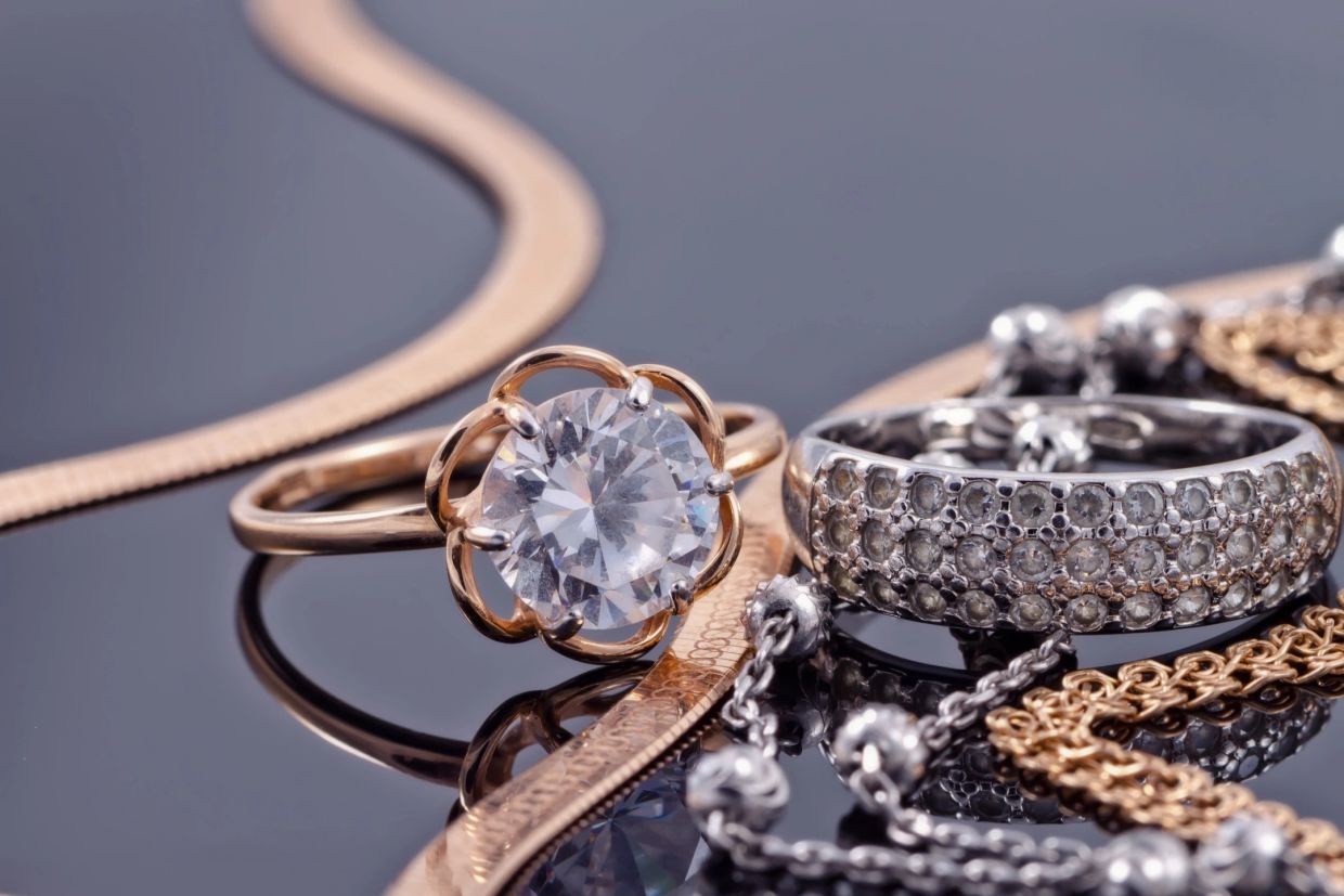Close-up of elegant rings and chains on reflective surface.