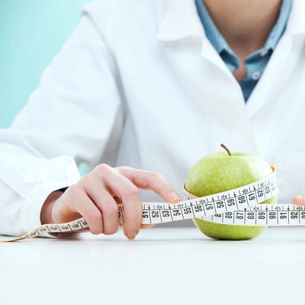 Person in lab coat measuring a green apple with a tape measure.