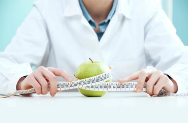 Person in white coat measuring a green apple with a tape measure.