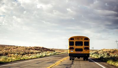 A yellow school bus driving on an empty road under a cloudy sky.