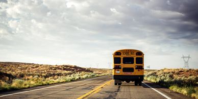 A yellow school bus driving on an empty road under a cloudy sky.
