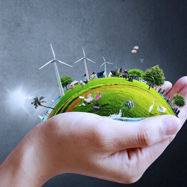 A hand holding a tiny green planet with wind turbines and animals.