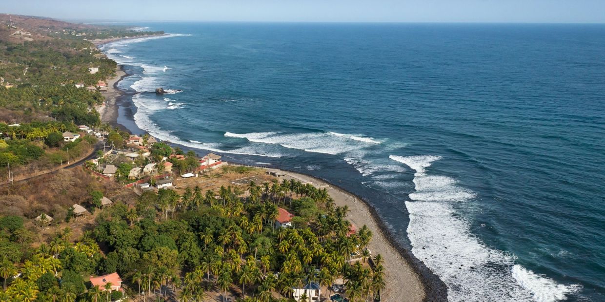A coastal village with lush greenery and waves crashing onto the shore.
