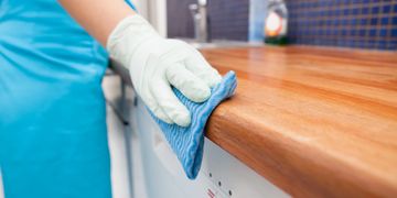 Person cleaning a wooden countertop with a blue cloth.