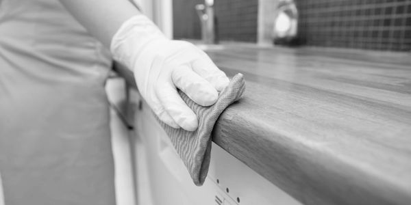 Person cleaning a wooden kitchen countertop with a cloth and gloves.