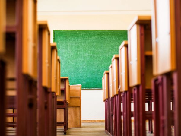 Empty classroom with wooden desks and a green chalkboard.