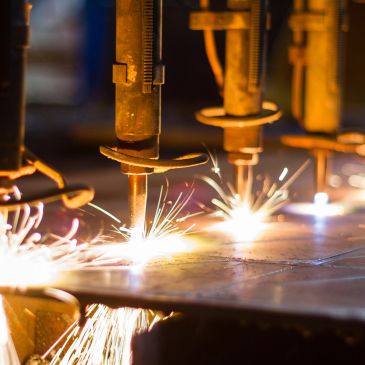 Automated machines cutting metal with bright sparks flying.