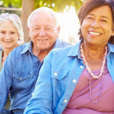 Three seniors smiling outdoors, enjoying a sunny day.