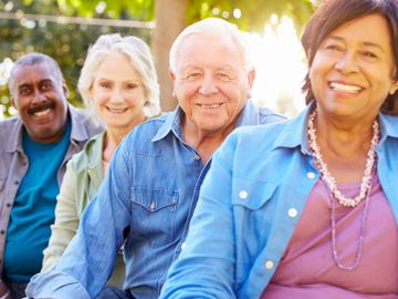 Four older person sitting in a row smiling from different ethnic backgrounds