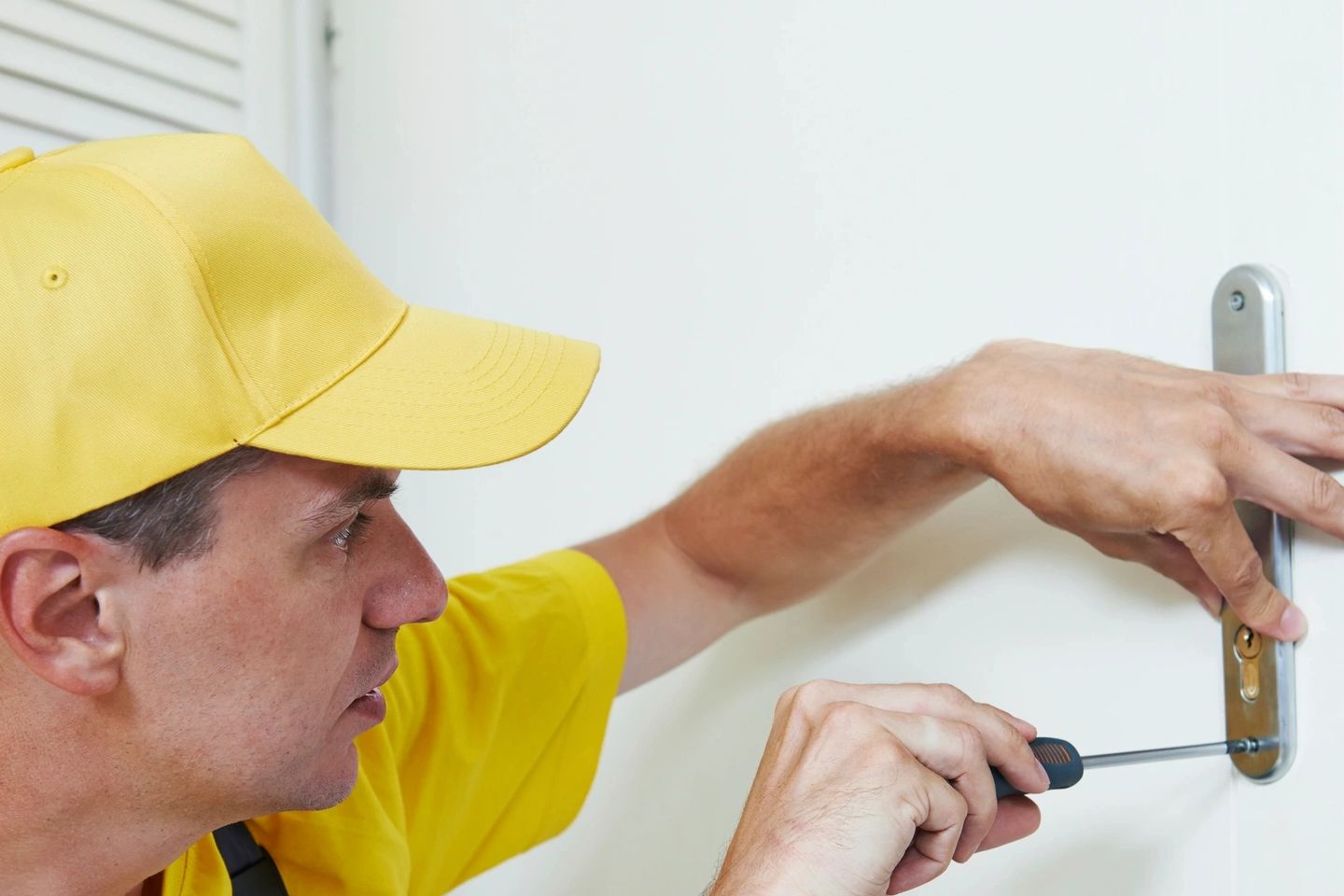A man in yellow uniform fixing a door lock with a screwdriver.