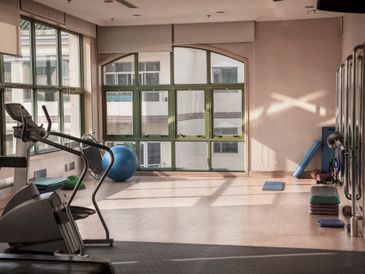 A room set up as a home gym with a cross trainer, exercise ball, weights and bench in it.