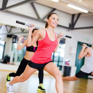 Group fitness class with participants doing lunges holding bars on their shoulders.