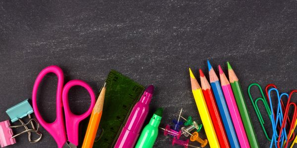 Colorful school supplies including scissors, pencils, markers, and paper clips on a chalkboard.