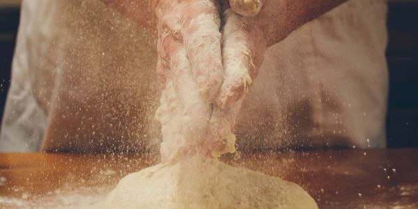 Hands kneading dough with flour dust in the air.