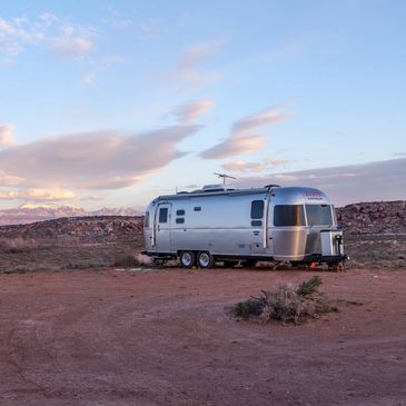 A silver Airstream trailer parked in a desert landscape under a cloudy sky.