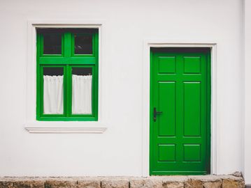 Green door and window on a white wall with stone base.