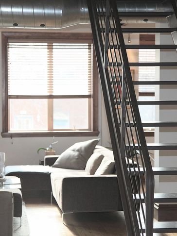 Modern living room with a gray sofa and metal staircase.