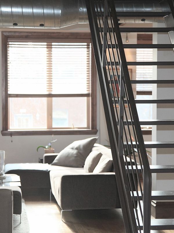 Modern living room with a gray sofa and metal staircase.