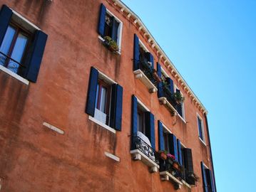 Exterior of a rustic brick building with blue shutters and flower boxes under a clear blue sky.