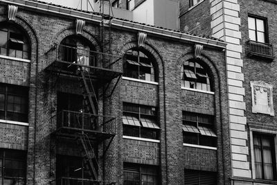 Black and white photo of an old brick building with fire escape and arched windows.