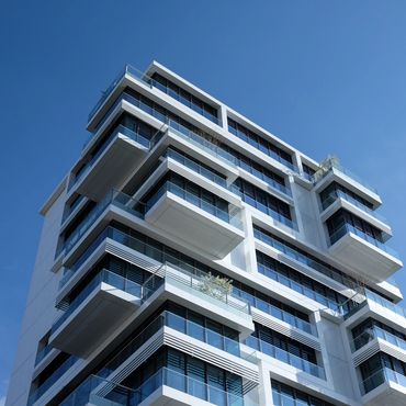 Modern multi-story building with glass balconies and a clear blue sky.