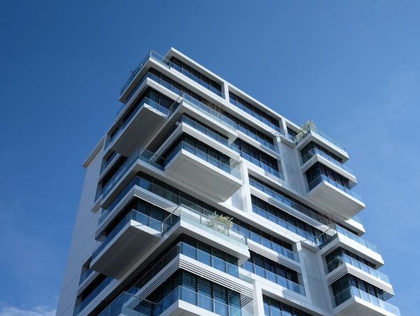 Modern high-rise building with glass balconies under clear blue sky.