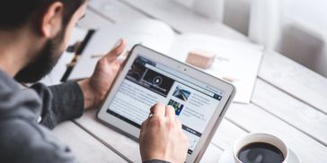 Person reading news on a tablet with coffee nearby.