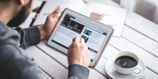 A person working on his smart tablet and drinking coffee