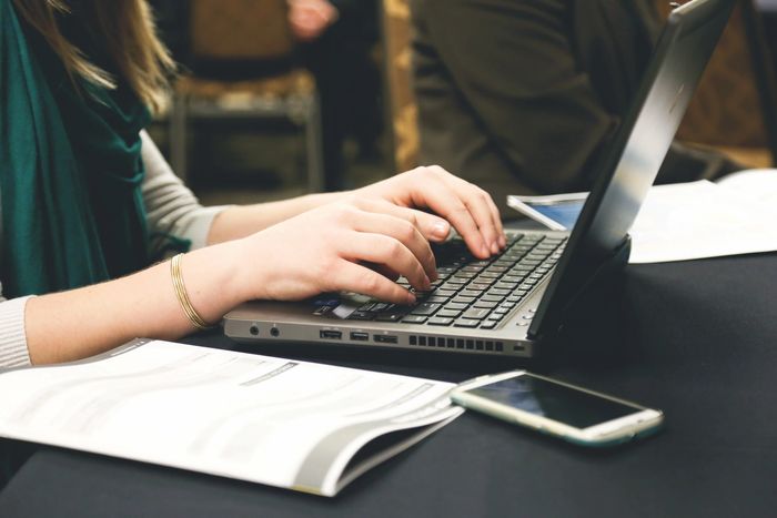 a woman typing on a laptop and writing something.