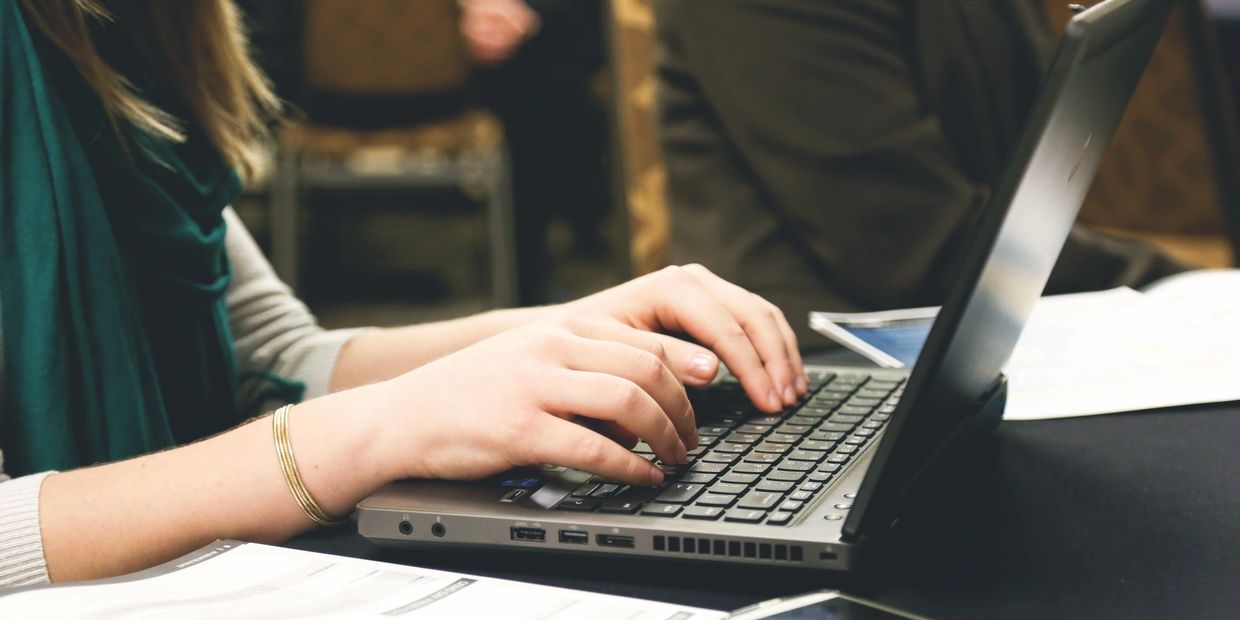 Person typing on a laptop with documents and a smartphone nearby.