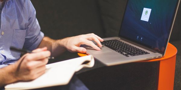 A view of a person’s one hand touching the laptop and the other hand holding a ball pen