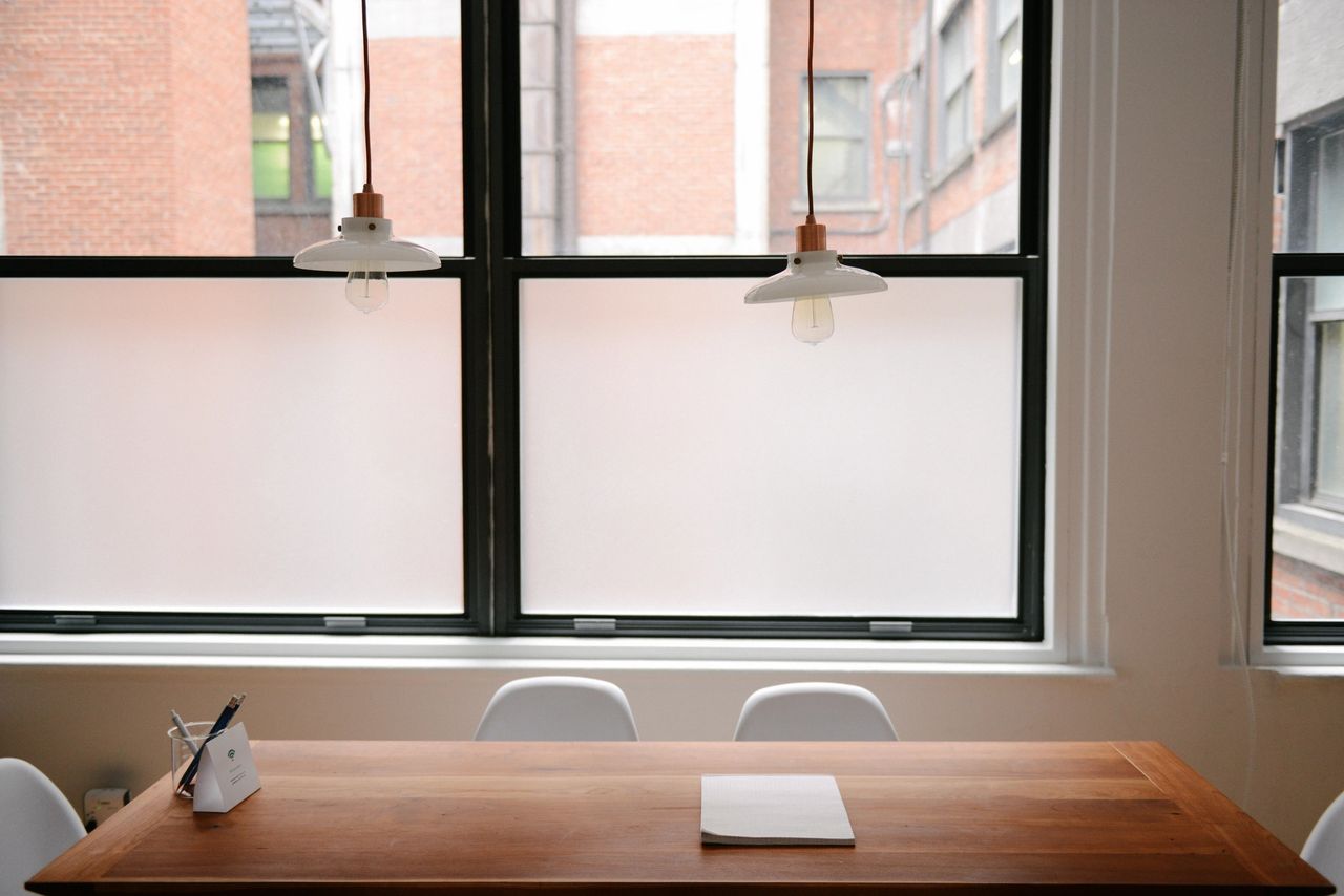 Modern workspace with wooden table, white chairs, and pendant lights, featuring a notepad and pen, illustrating a professional setting for event planning in NYC.