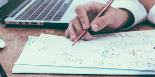 Image shows one set on hands with a pencil and paper and one set of hands near laptop.