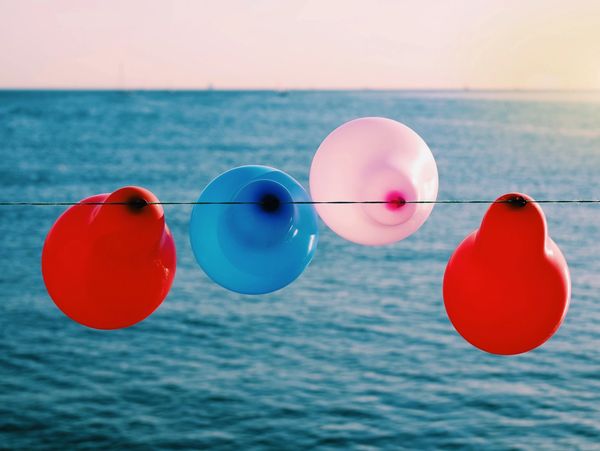 Red, blue and pink balloons hanging on a string with the ocean view behind them