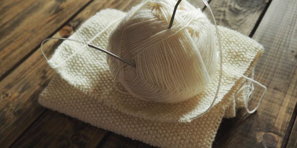 Ball of white yarn and knitting needles on knitted fabric.