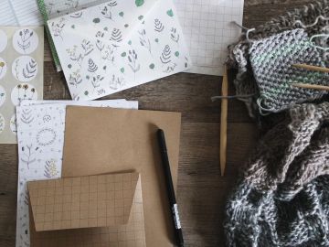 Crafting materials including knitting wool, patterned papers, and a pen on a wooden table.