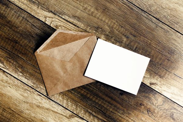 A blank card next to an open brown envelope on a wooden surface.