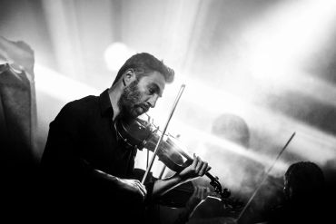 Man playing violin in dramatic black and white lighting.
