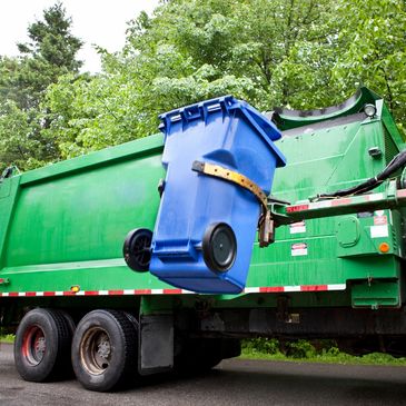 Green garbage truck lifting a blue trash bin for emptying.