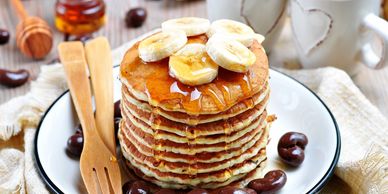 Stack of pancakes topped with banana slices and syrup on a white plate.