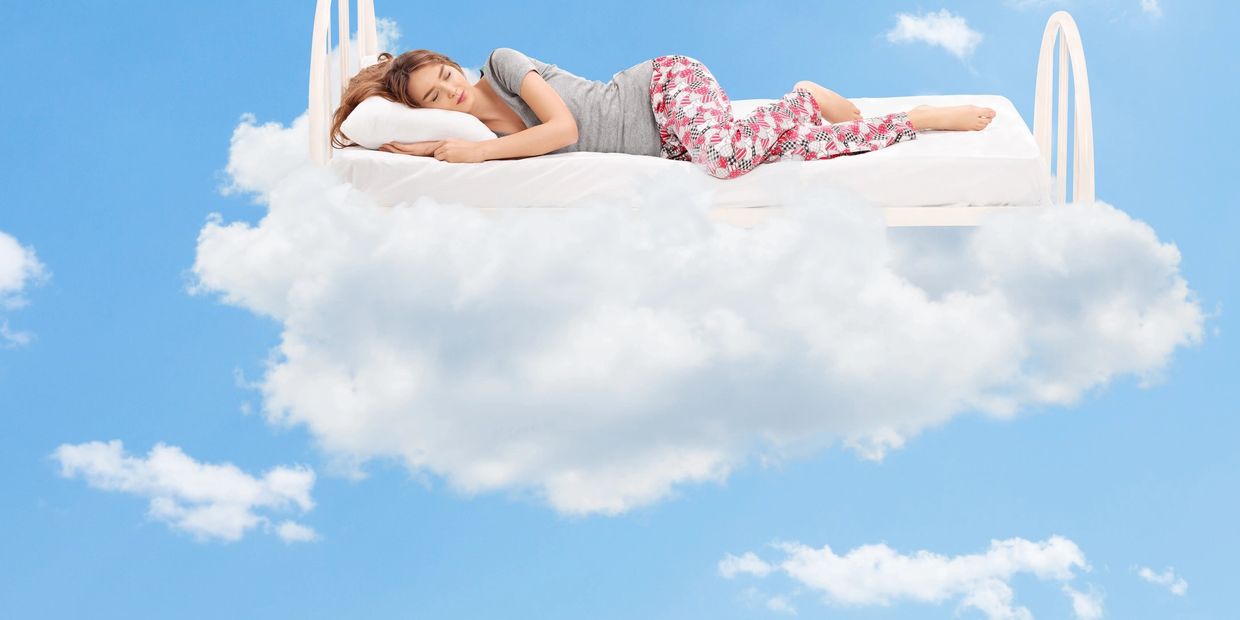 woman sleeping on a mattress, pillow, and bed frame on a cloud in the sky